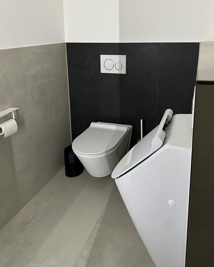 Modernes Badezimmer mit hellgrauen und anthrazitfarbenen Fliesen, hängender Toilette und Urinal