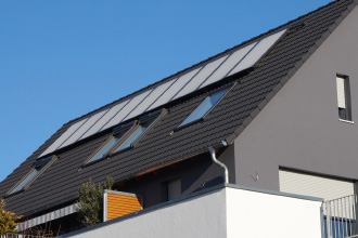 Ein modernes graues Wohnhaus vor blauem Himmel und Solaranlage auf dem Dach